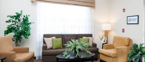 A living room with a brown sofa, two armchairs, a coffee table, and potted plants.