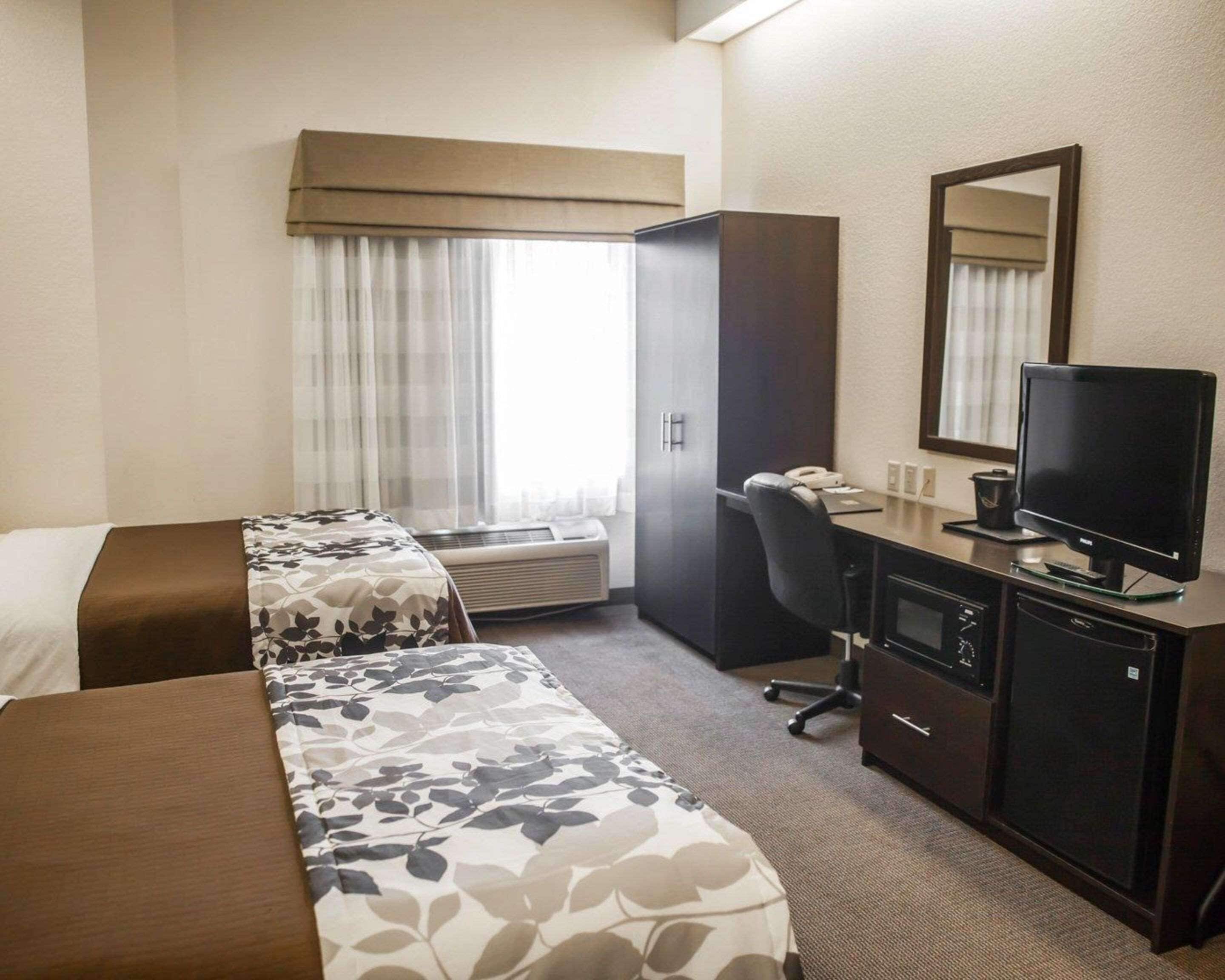 A hotel room with two beds, a desk with a computer, a television, and a wardrobe.