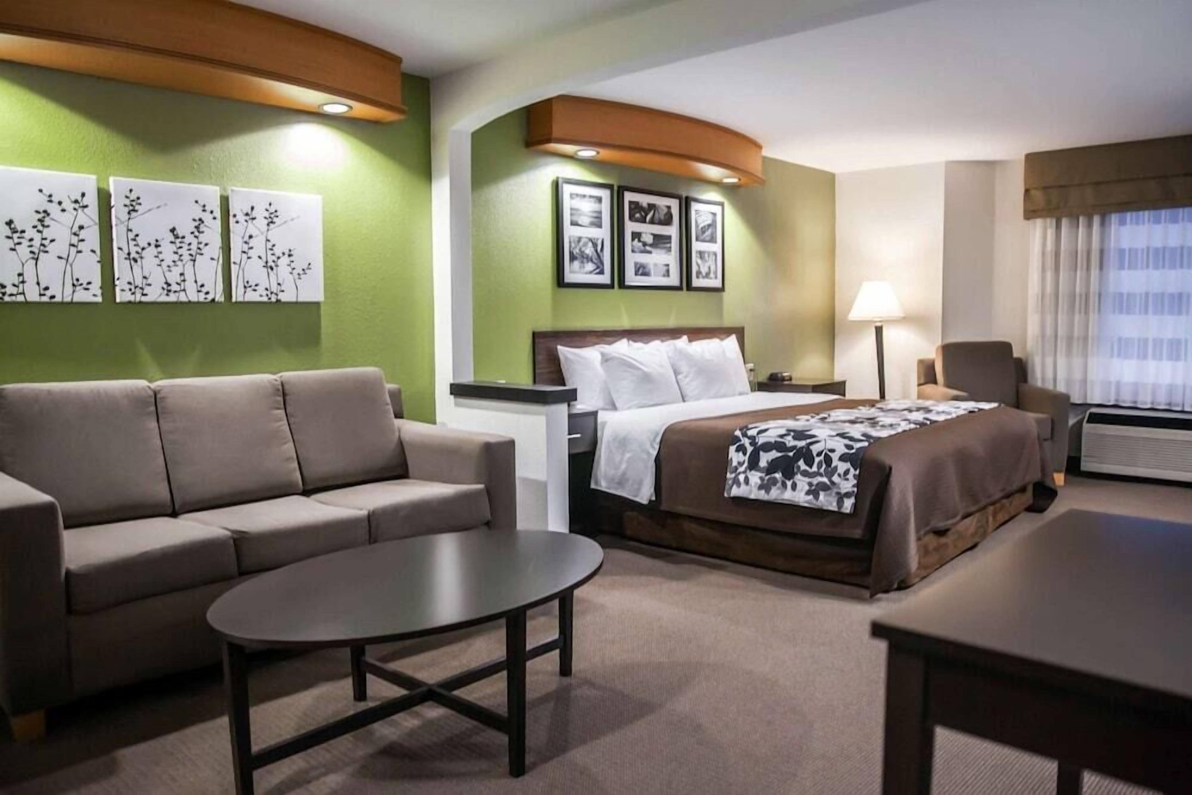 A hotel room with a bed, a sofa, a table, and artwork on the walls.