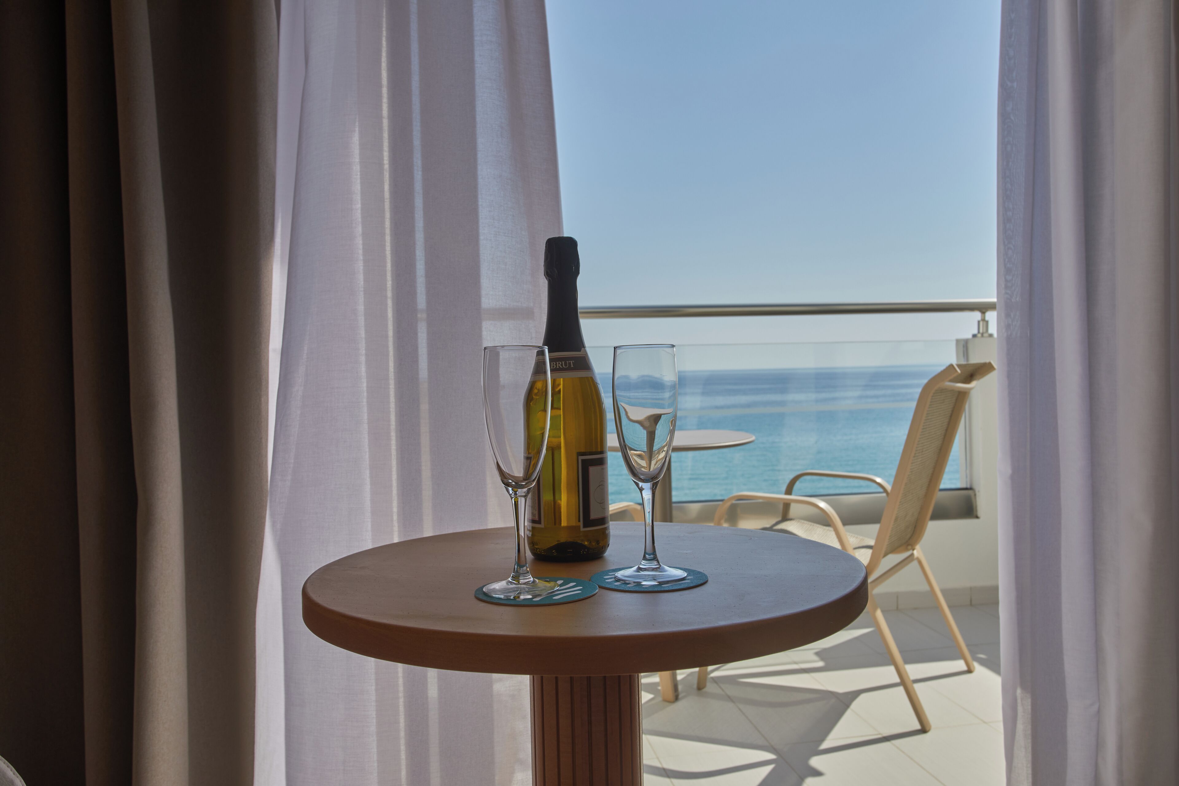 Un tavolo con una bottiglia di vino e due bicchieri su un balcone con vista sul mare.
