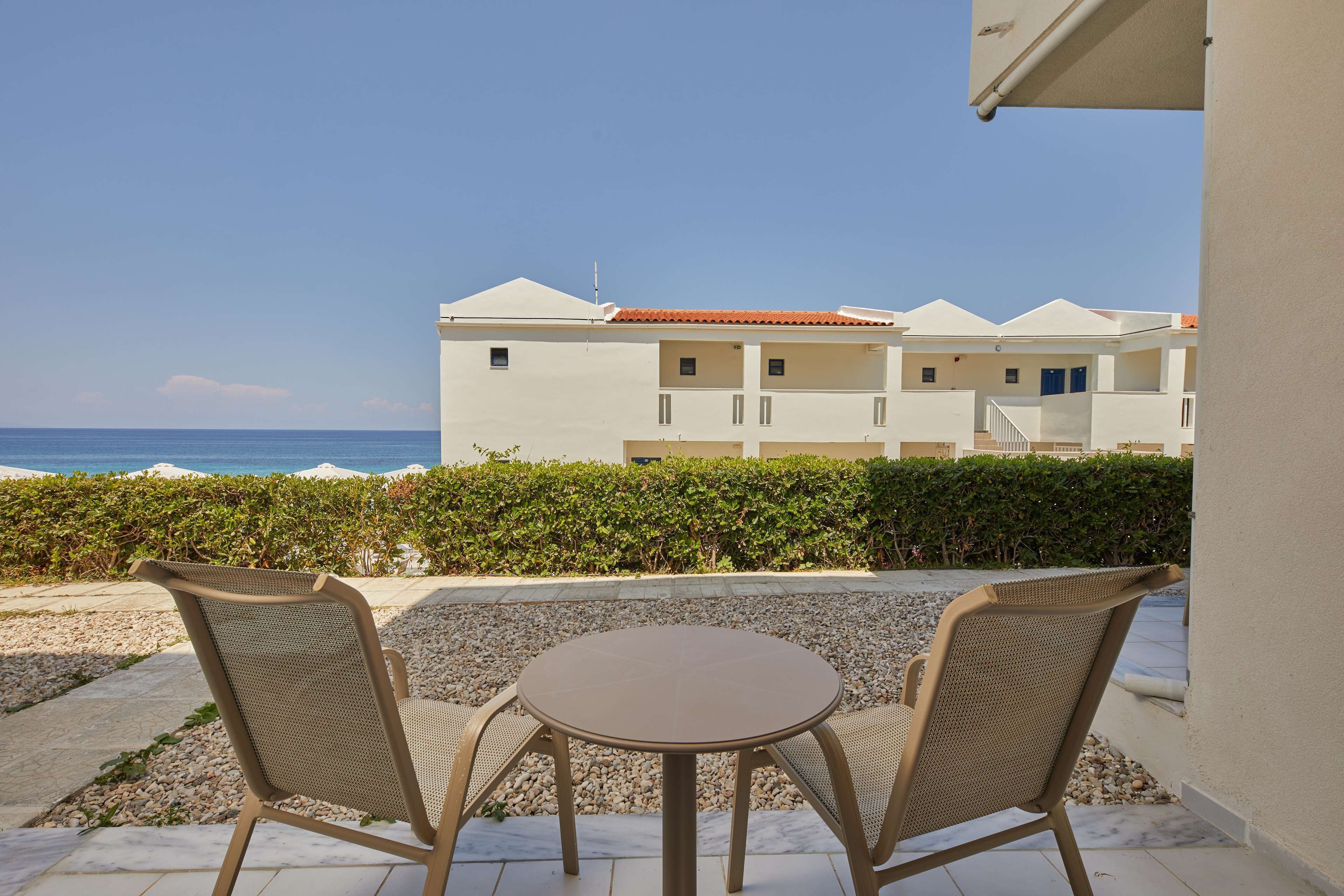 A patio with two chairs and a table, overlooking a beach and a building with multiple balconies.