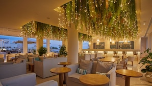 Un salón en la azotea con sofás, mesas redondas y plantas colgantes.