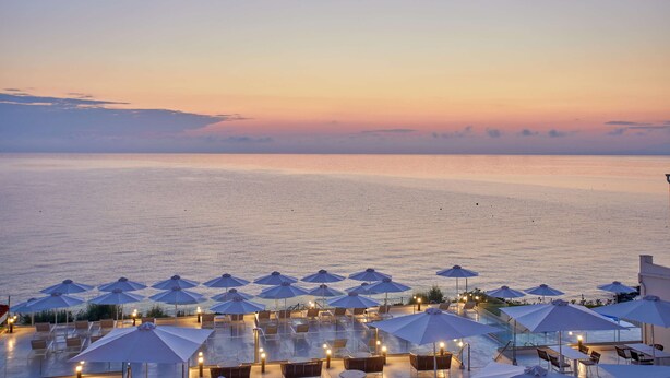 A resort with a pool area featuring umbrellas and lounge chairs, overlooking a calm sea at sunset. - AluaSoul Zakynthos - Adults Only - All Inclusive (Zakynthos)