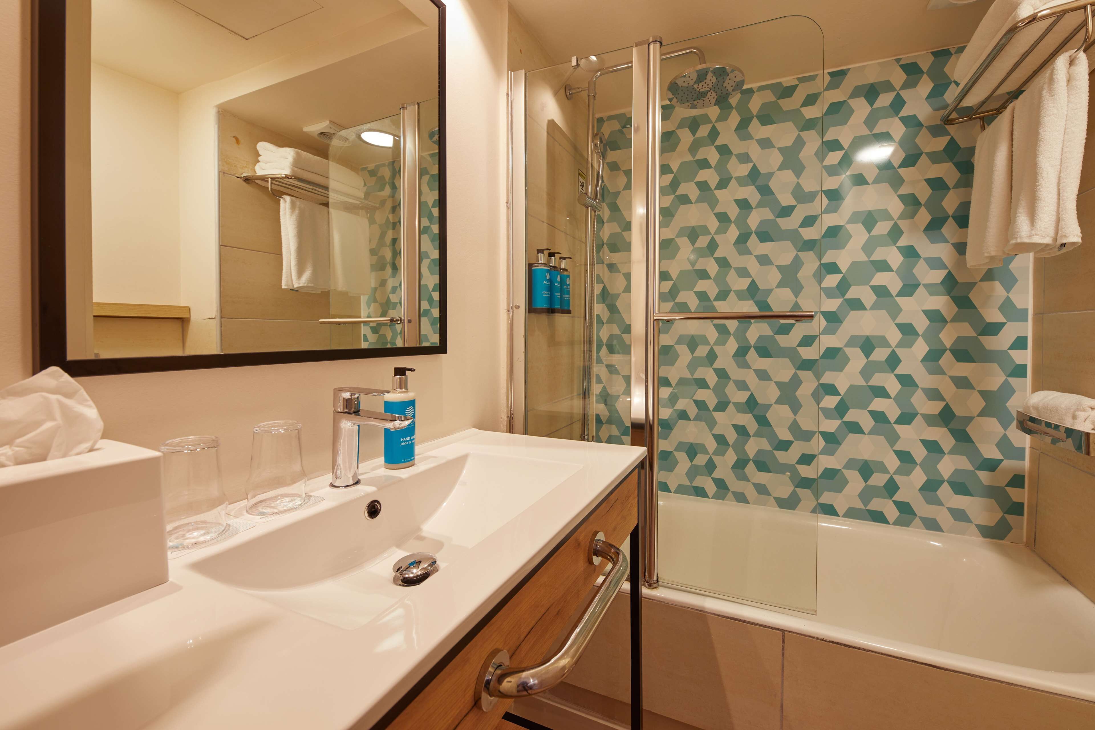 Une salle de bain moderne avec une douche à parois de verre, un lavabo blanc et un grand miroir.