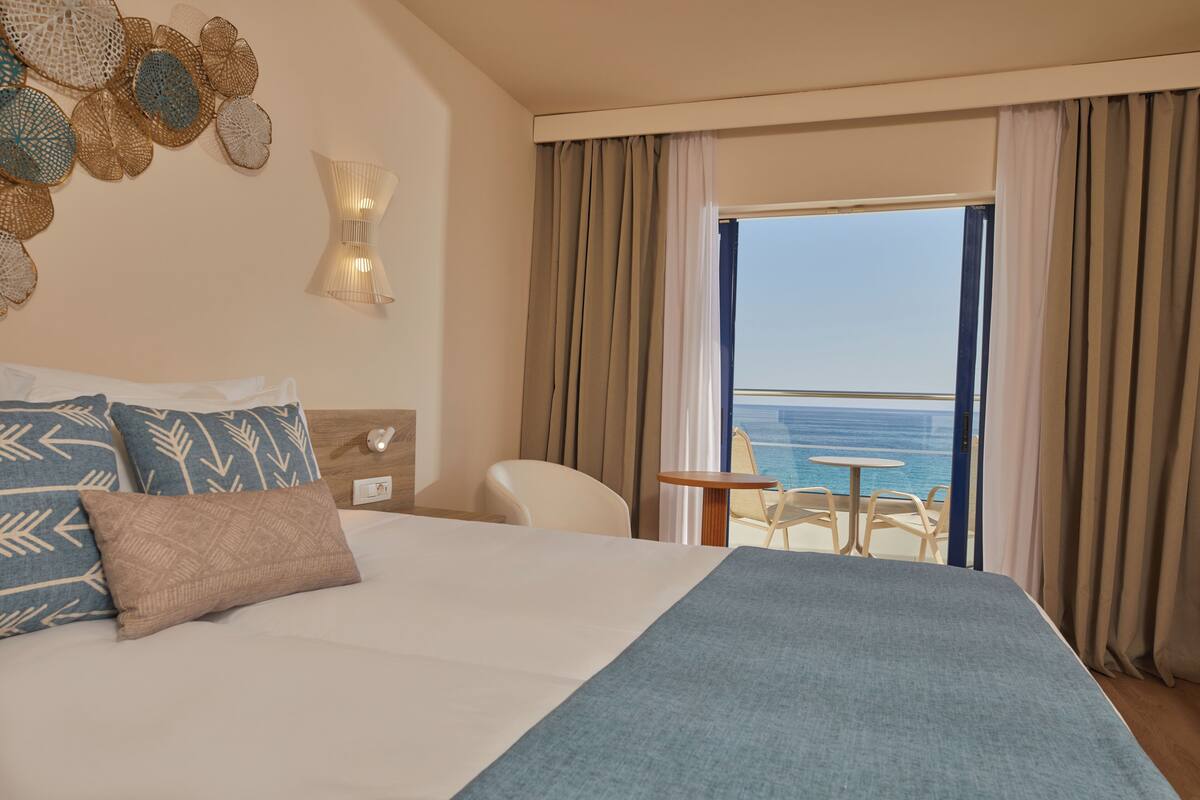 A hotel room with a large bed, a small table, a chair, and a view of the ocean.