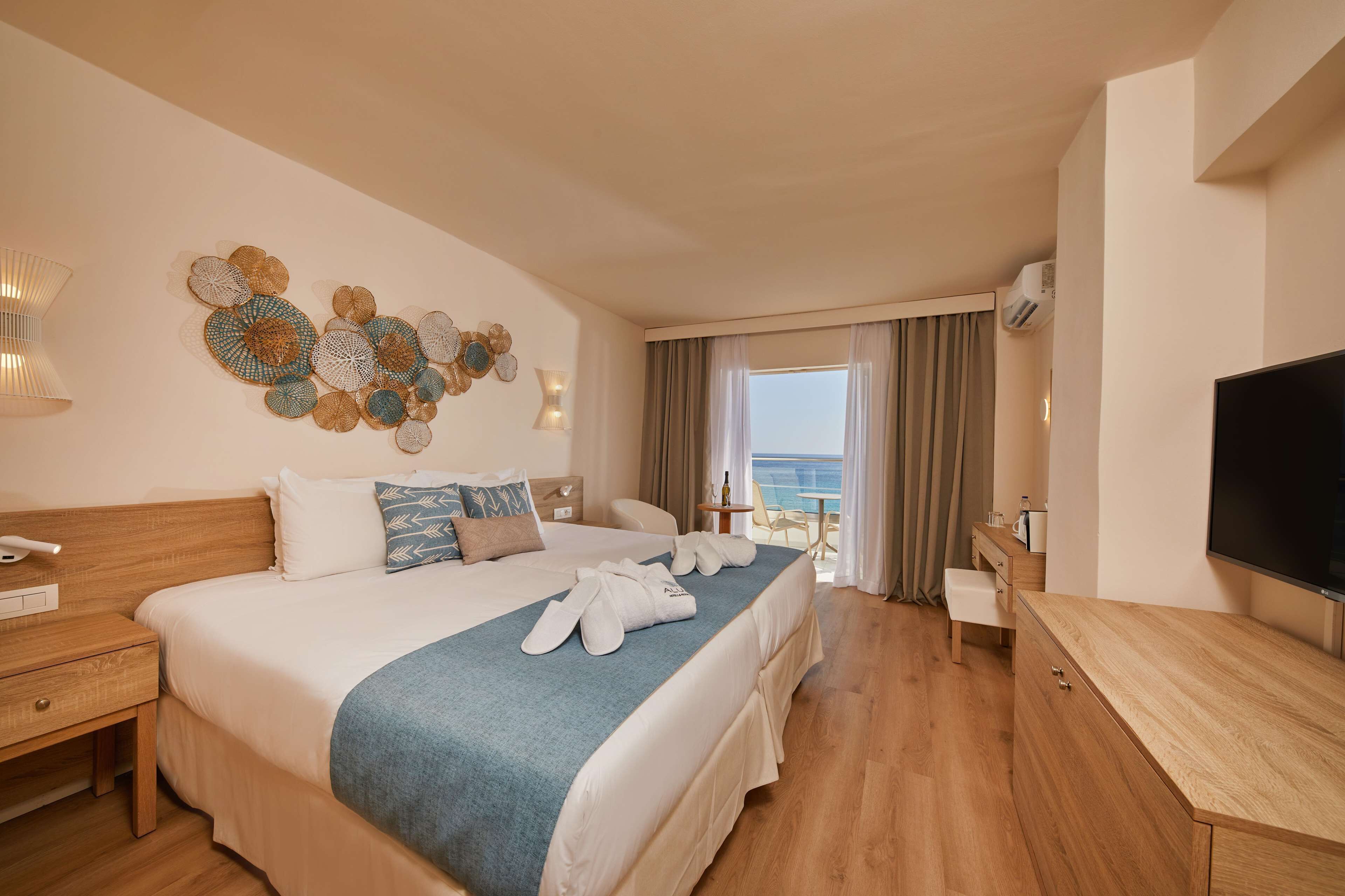 Une chambre d’hôtel avec un grand lit, une télévision, un bureau et un balcon donnant sur la mer.