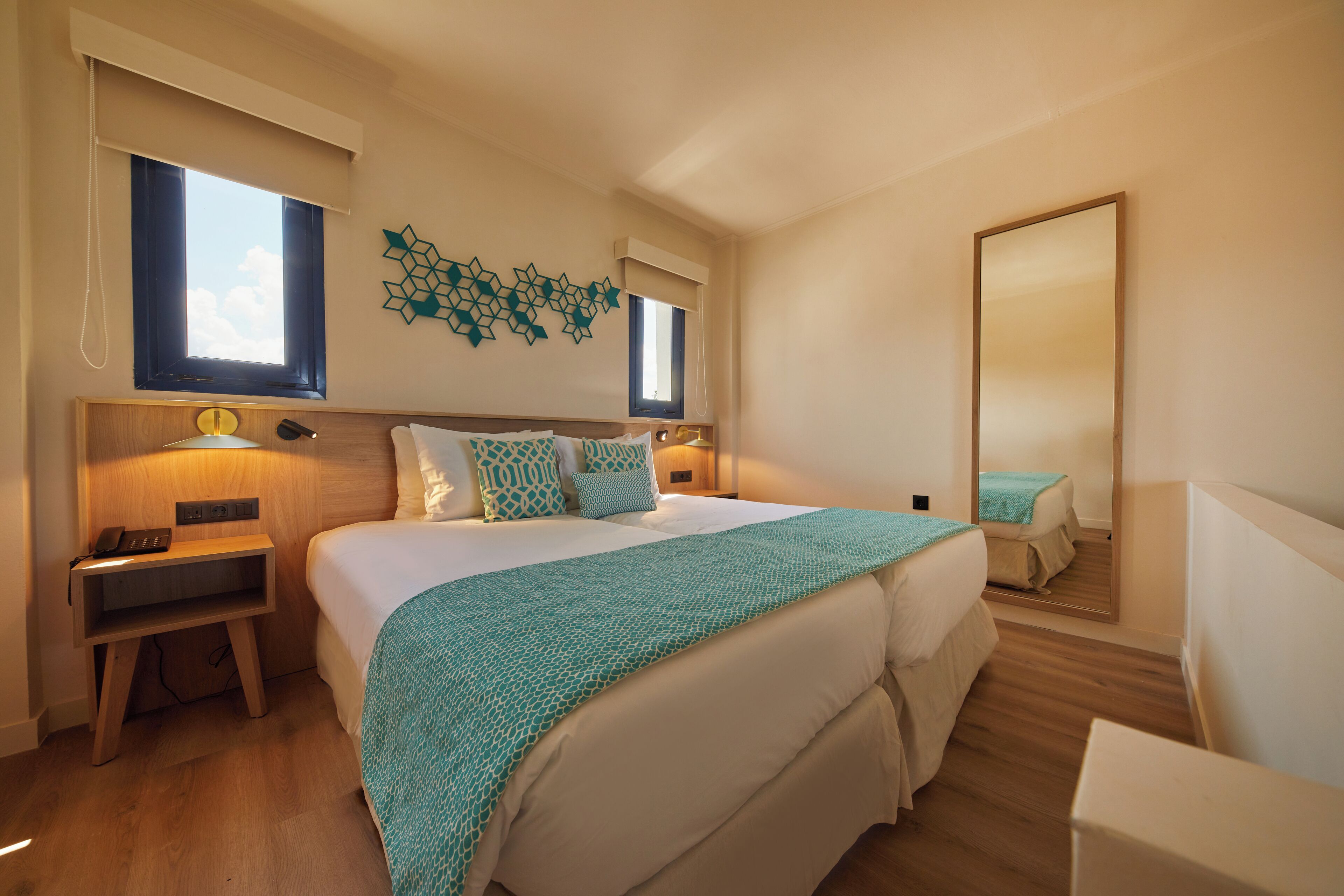 Een slaapkamer met een groot bed, nachtkastjes, een spiegel en een raam met jaloezieën.