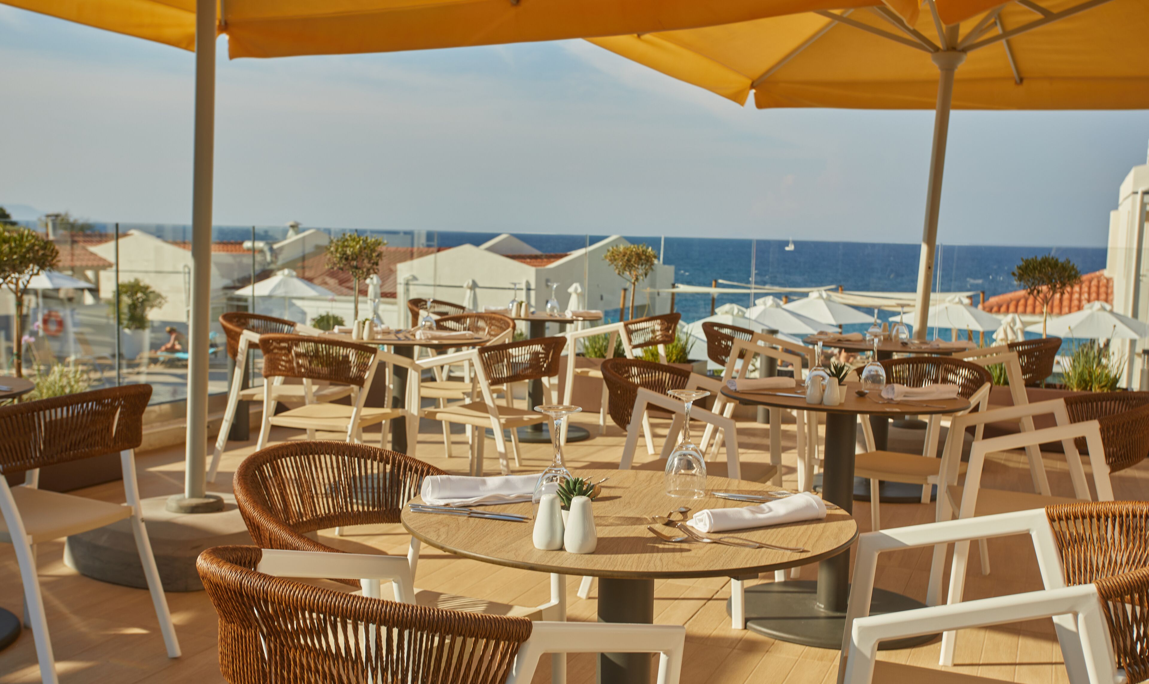 Un área de comedor al aire libre con sillas y mesas de mimbre, con vistas a la costa.