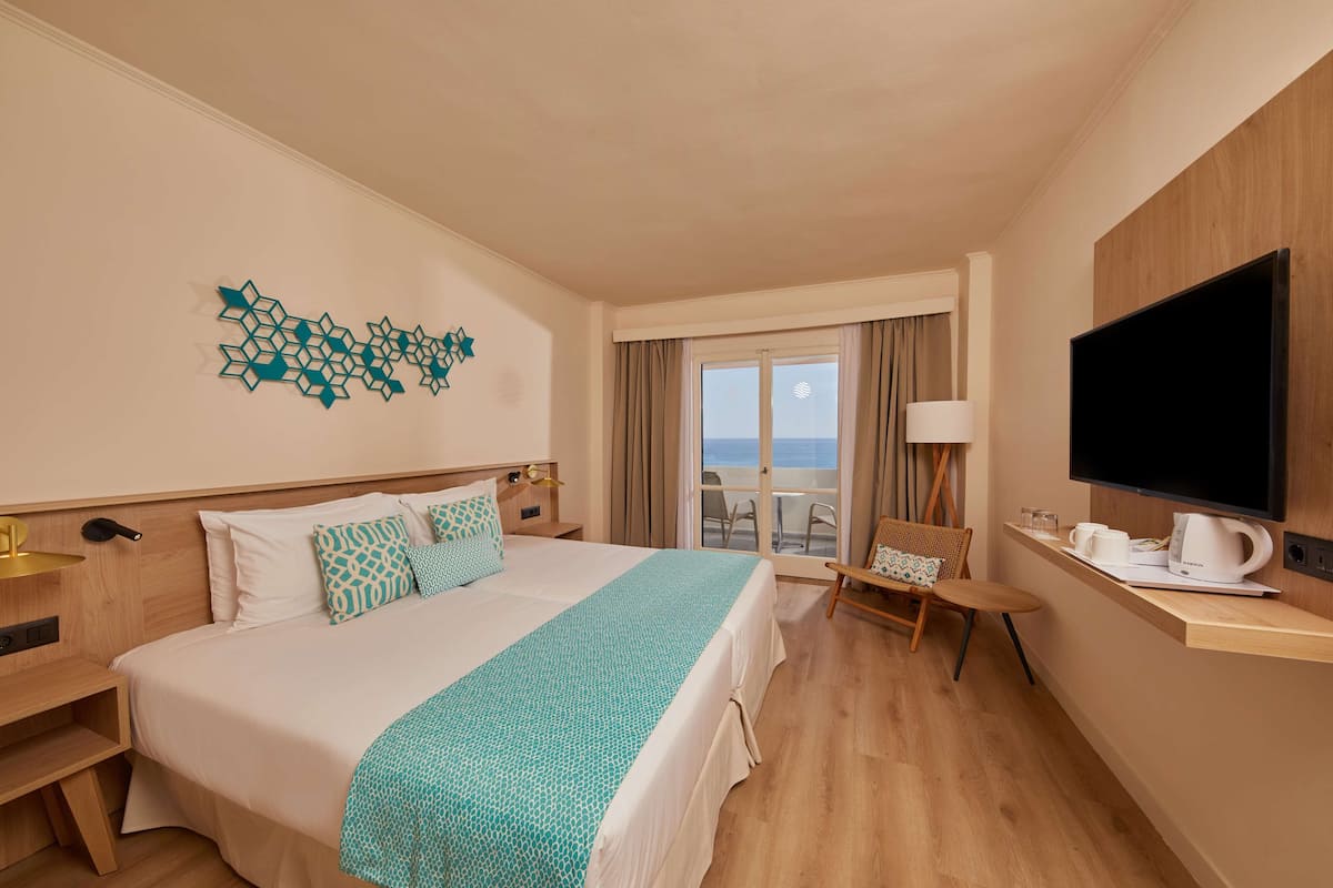 A hotel room with a bed, a TV, a coffee maker, and a view of the ocean.