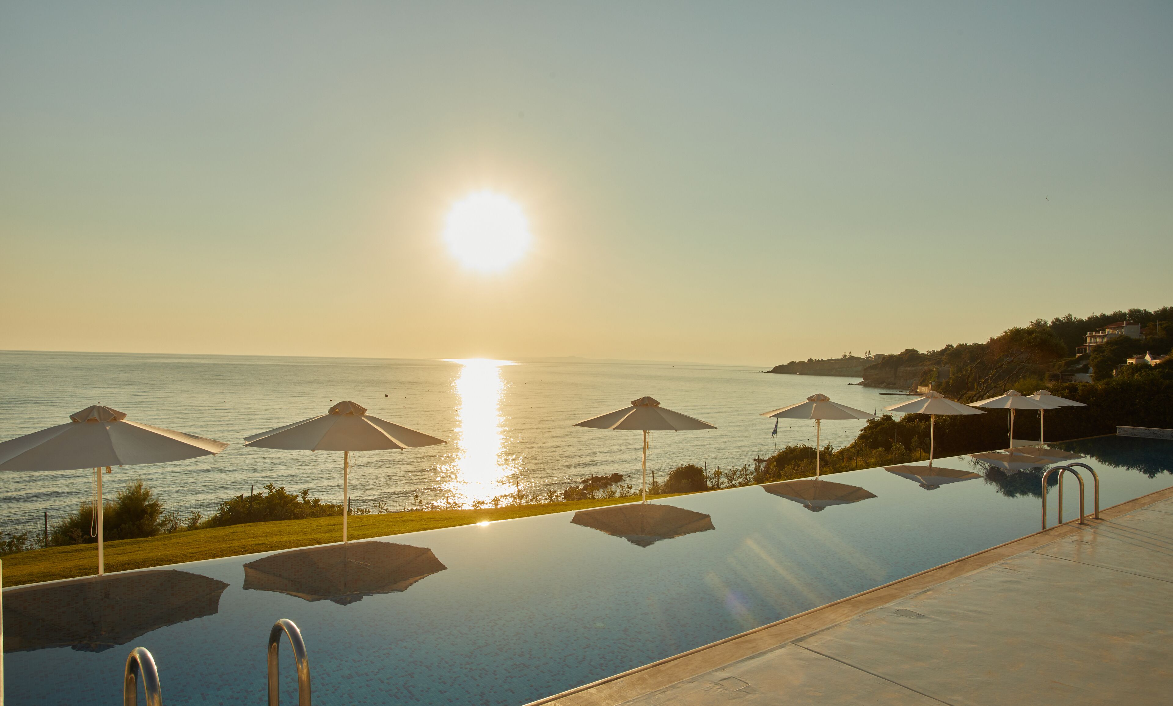 Una piscina con sombrillas y vistas despejadas al mar, con un paisaje montañoso de fondo.