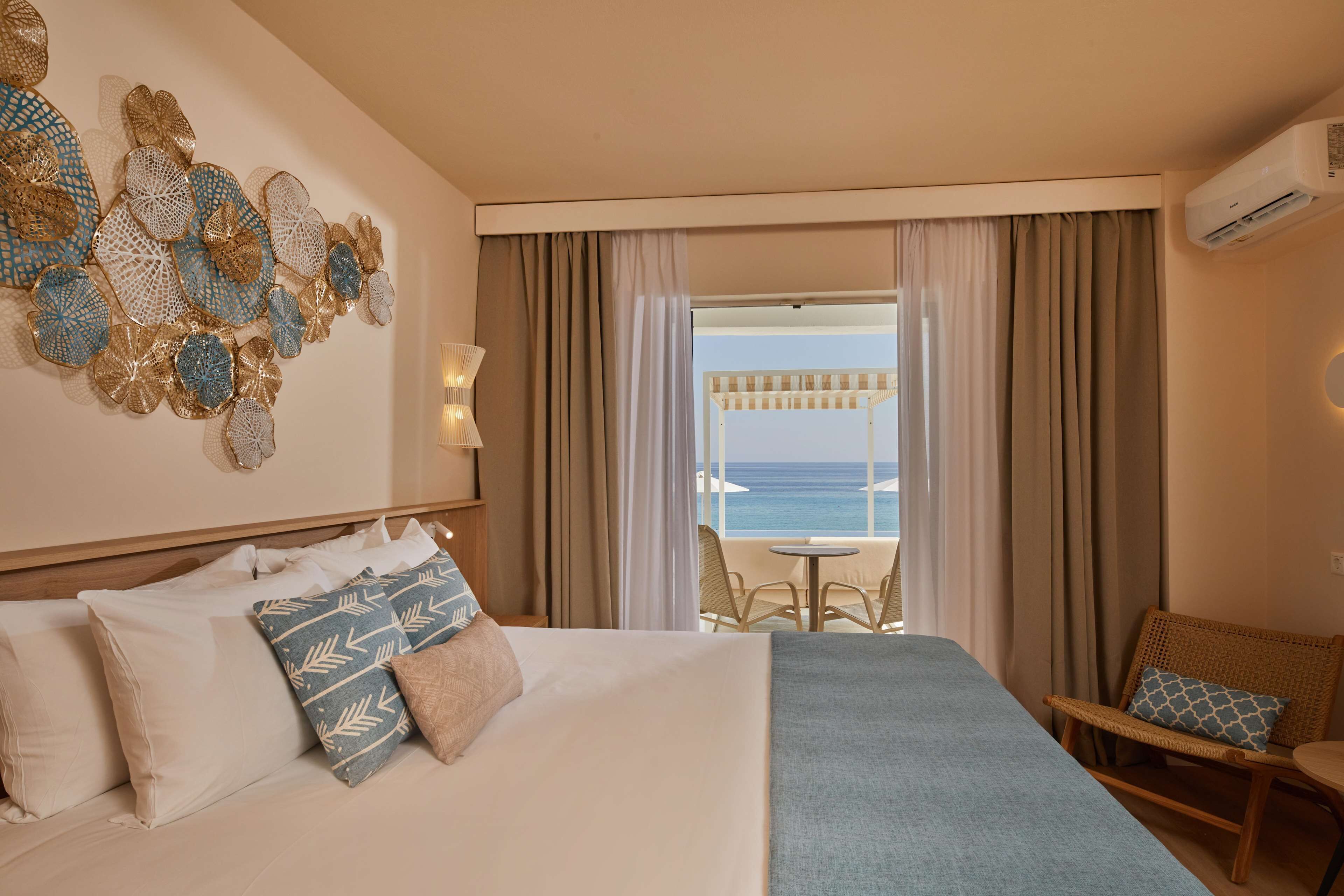 Una camera d'hotel con un letto grande, vista mare e un balcone con posti a sedere esterni.