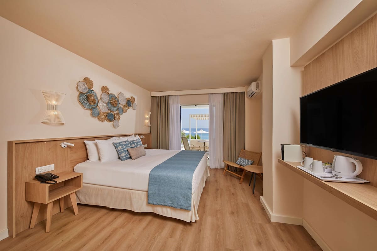 A hotel room with a bed, bedside tables, a TV, a desk, and a view of the outdoors.