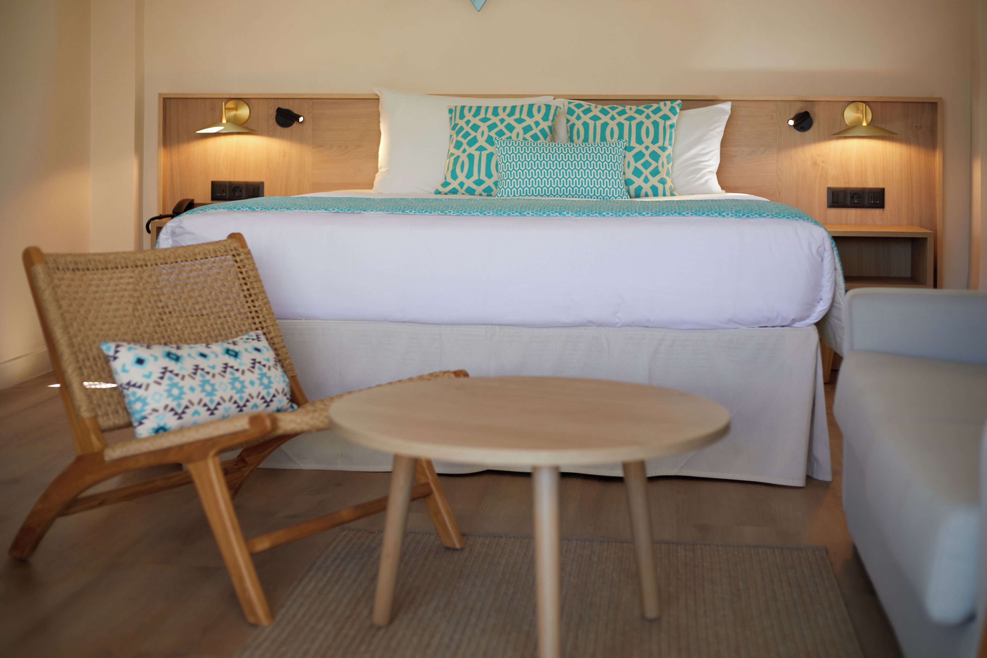 Quarto de hotel com uma cama, uma mesinha redonda e duas cadeiras de vime.