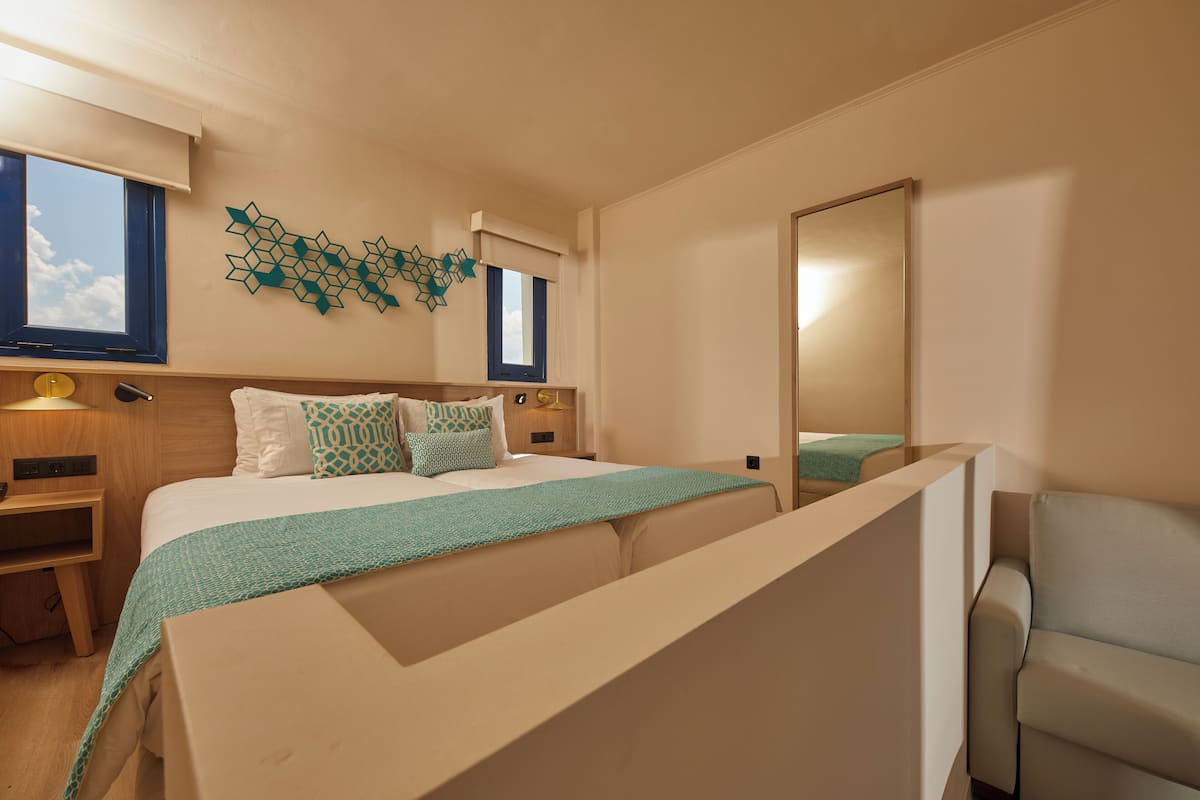 A modern hotel room with a bed, bedside tables, a mirror, and a view of the sky through the window.