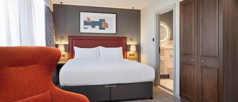 Habitación de hotel con una cama grande, un sillón rojo, un armario y un cuadro en la pared.