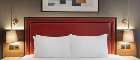 A hotel room with a red upholstered headboard, white bedding, and two bedside lamps.