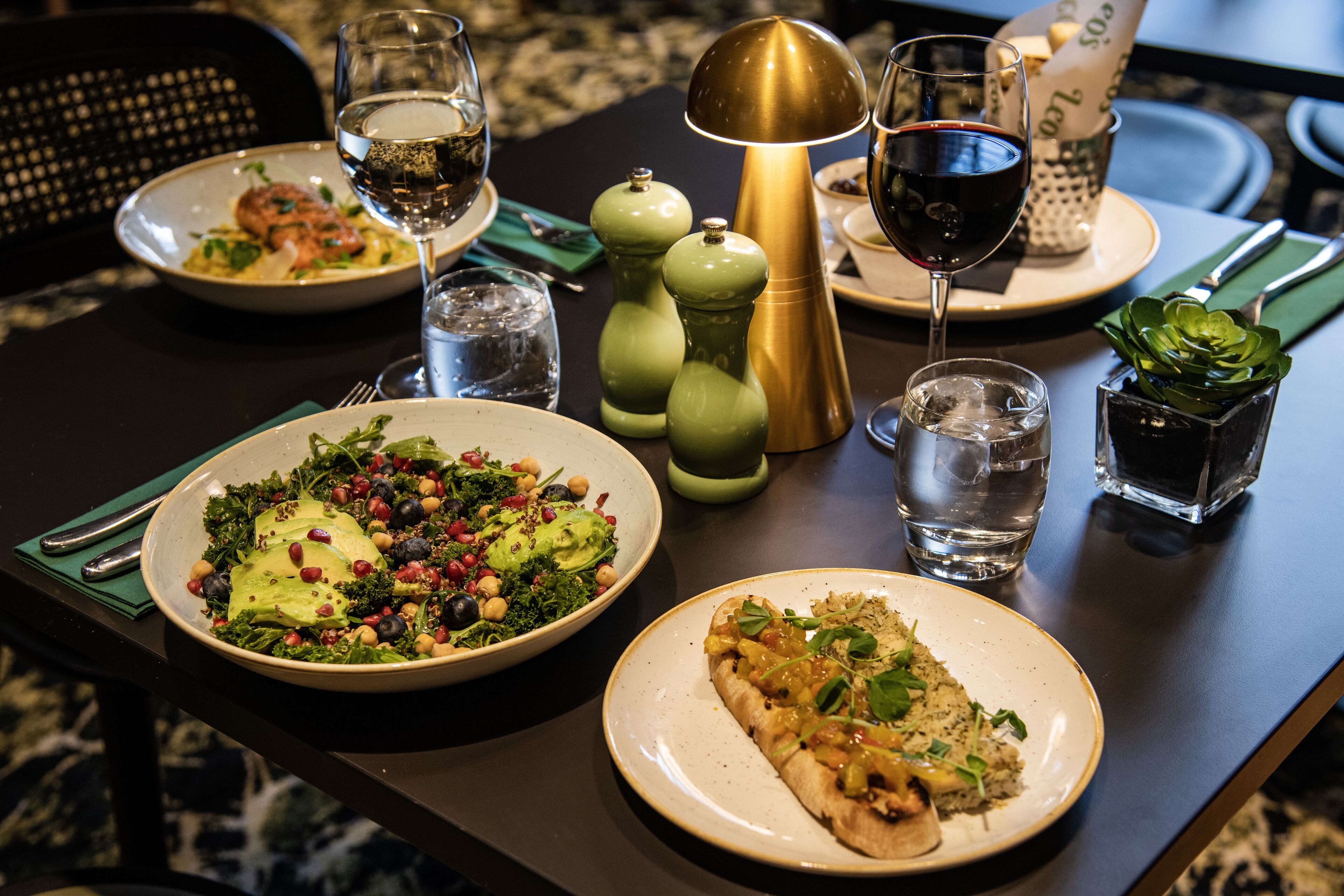 A dining table with plates of food, glasses of water and wine, and a decorative lamp.