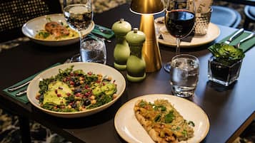 Una mesa de comedor con platos de comida, vasos de agua y vino, y una lámpara decorativa.