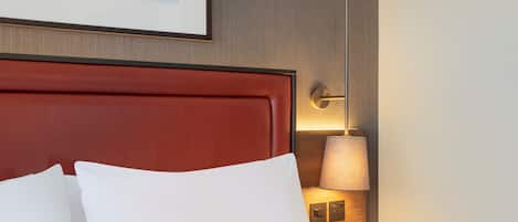 Habitación de hotel con cama, cabecero, mesita de noche, lámpara y un cuadro en la pared.