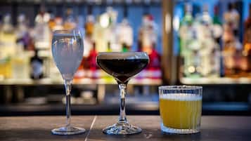 Tres vasos de bebidas distintas sobre una barra, con un fondo borroso de botellas.