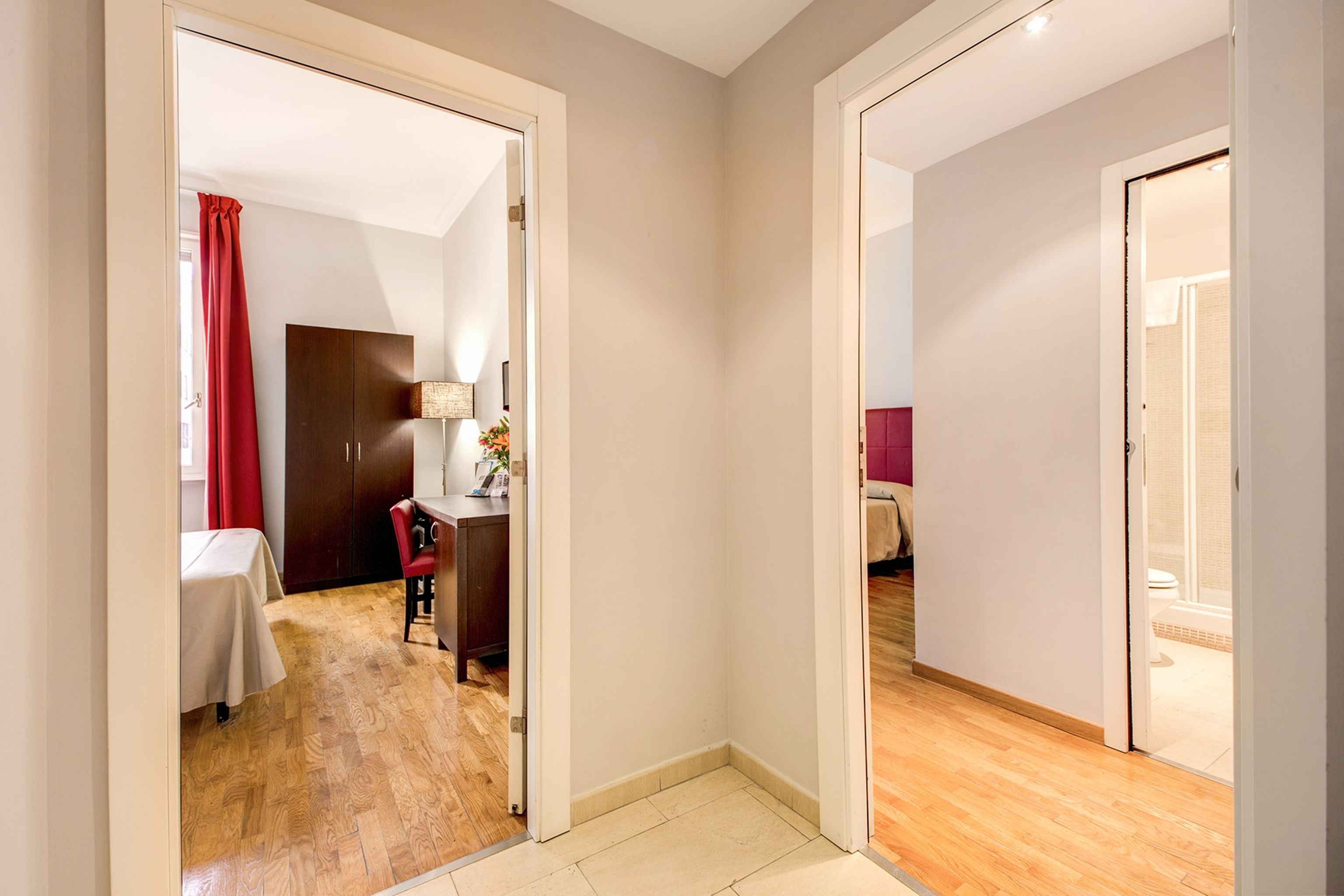 Habitación de hotel con piso de madera, un escritorio con silla, una cama y un baño visible a través de una puerta abierta.