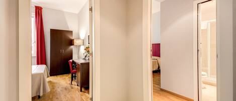 Habitación de hotel con piso de madera, un escritorio con silla, una cama y un baño visible a través de una puerta abierta.
