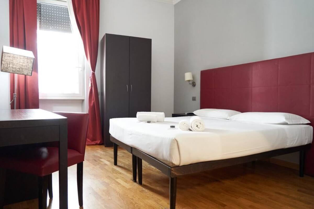 A hotel room with a bed, a desk, a wardrobe, and a window with curtains.