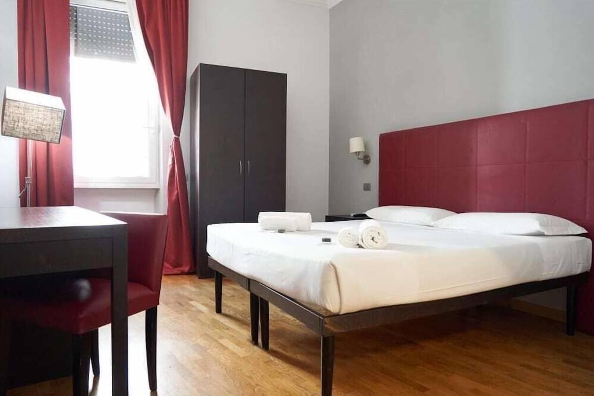 A hotel room with a bed, a desk, a wardrobe, and a window with curtains.