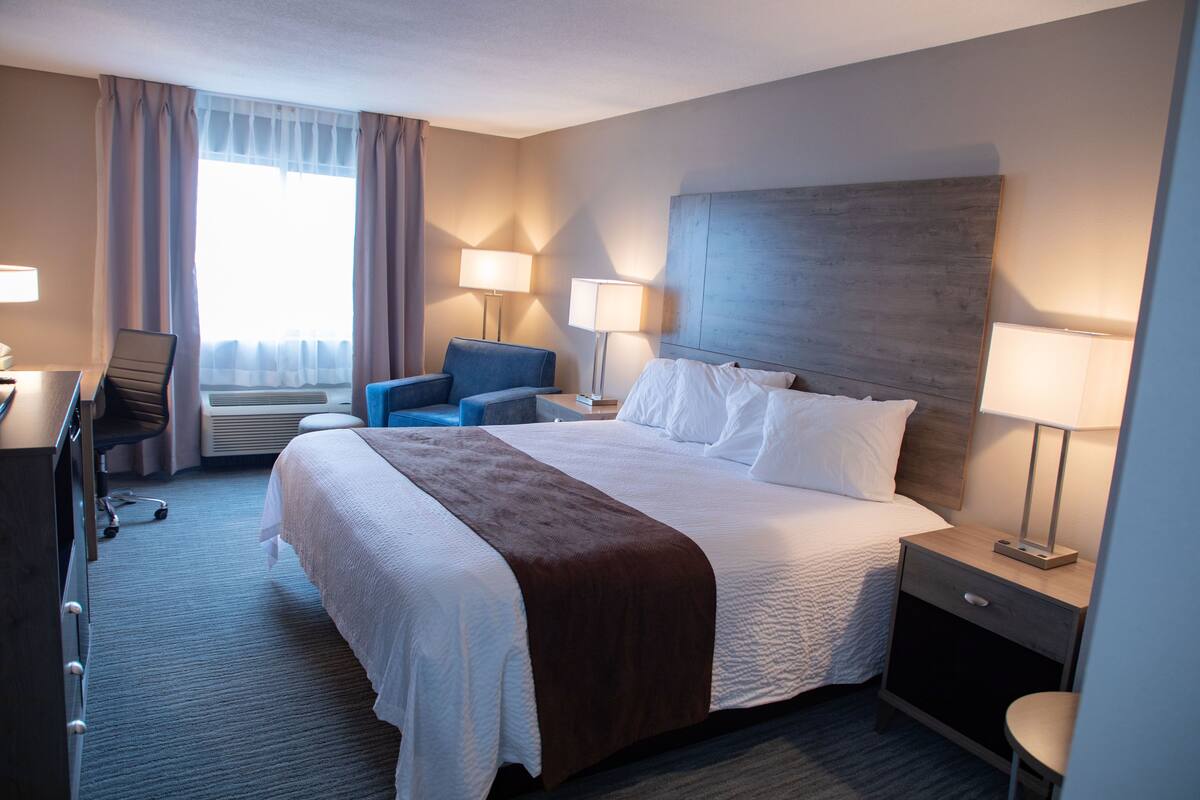 Een hotelkamer met een groot bed, twee bedlampen, een bureau met een stoel, een klein tafeltje en een raam met gordijnen.