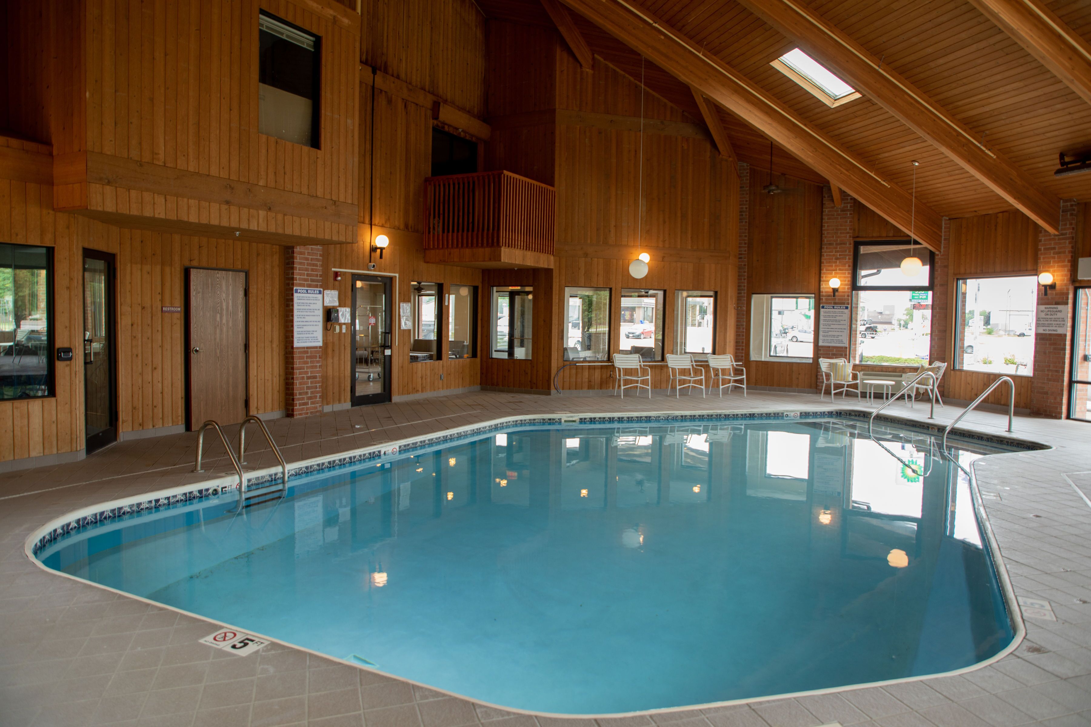 Una piscina interior con paredes y techo de madera, rodeada de zonas de estar y ventanas.