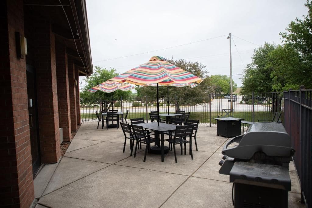 Un patio al aire libre con mesas y sillas, una parrilla y sombrillas a rayas.