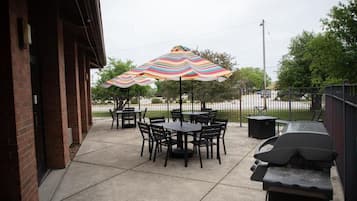 Un patio al aire libre con mesas y sillas, una parrilla y sombrillas a rayas.