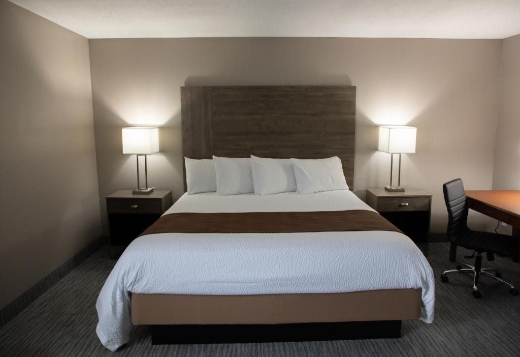 Habitación de hotel con una cama grande, dos mesitas de noche con lámparas, un escritorio y una silla.