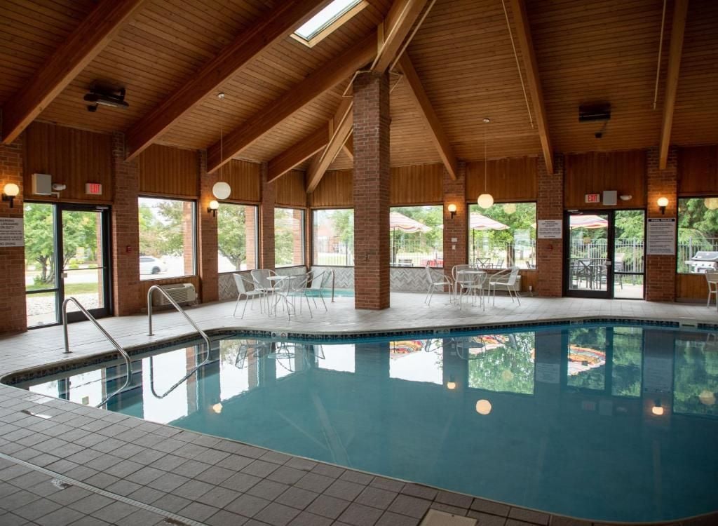 An indoor swimming pool with clear glass walls, wooden beams, and a tiled floor.