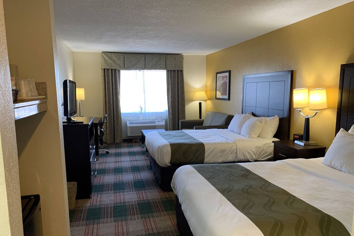 Une chambre d’h ôtel avec deux lits, un bureau, une chaise, une télévision et une fenêtre avec des rideaux.