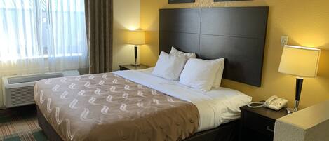 Une chambre d’hôtel avec un grand lit, deux lampes de chevet, un téléphone et une fenêtre avec des rideaux.