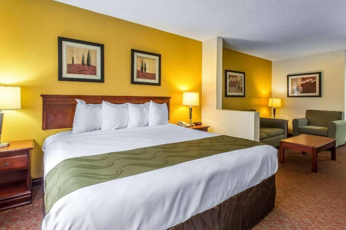Une chambre d’hôtel avec un grand lit, deux fauteuils, une petite table et deux lampes de chevet.