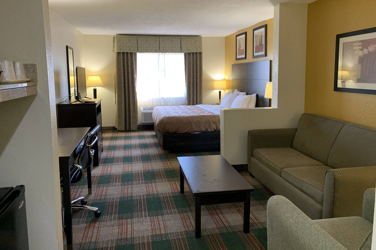 Une chambre d’hôtel avec un lit, un bureau, une chaise, un canapé et une petite table.