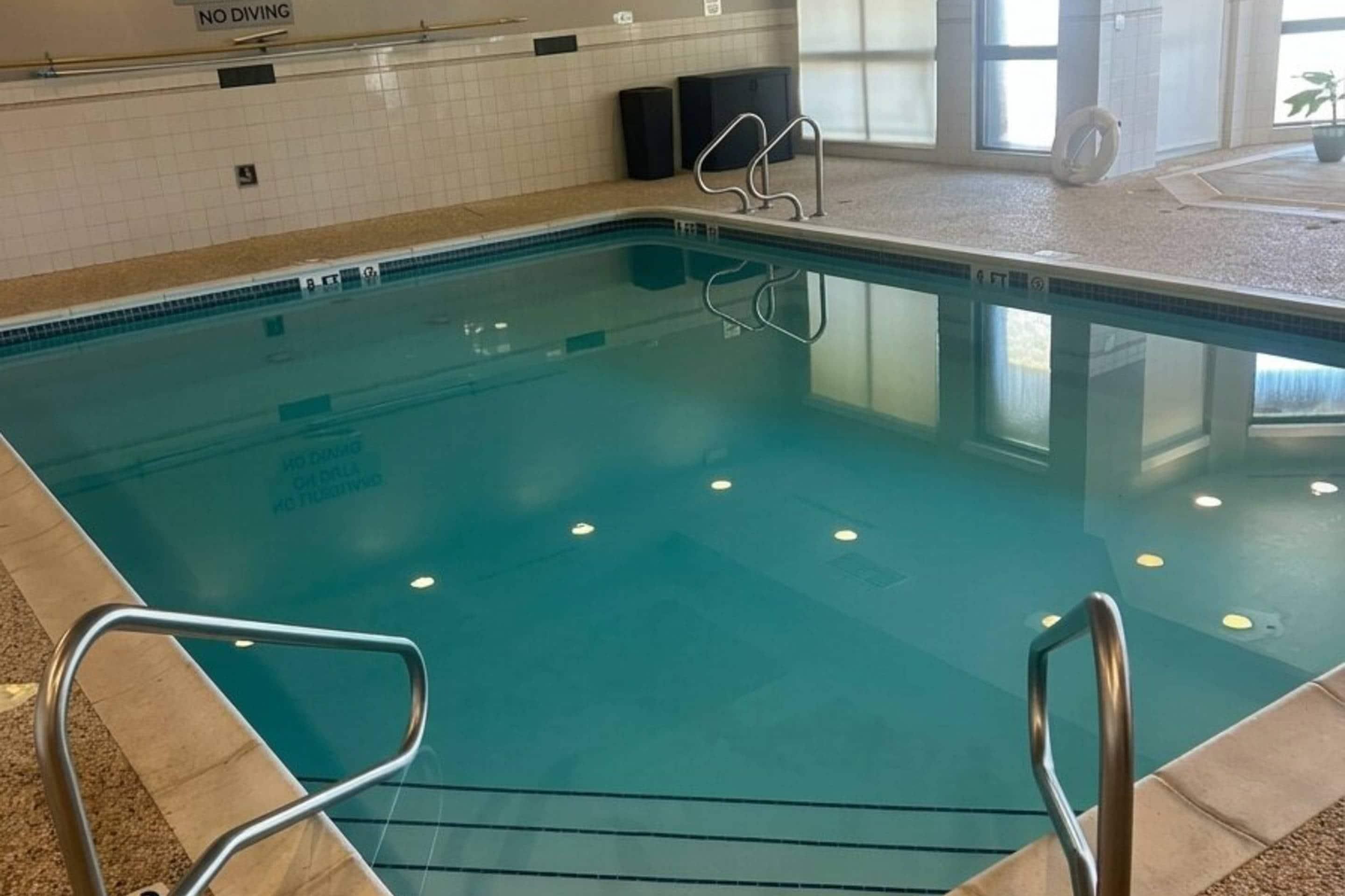 An indoor swimming pool with clear water, metal pool ladders, and a tiled wall with a 'NO DIVING' sign.