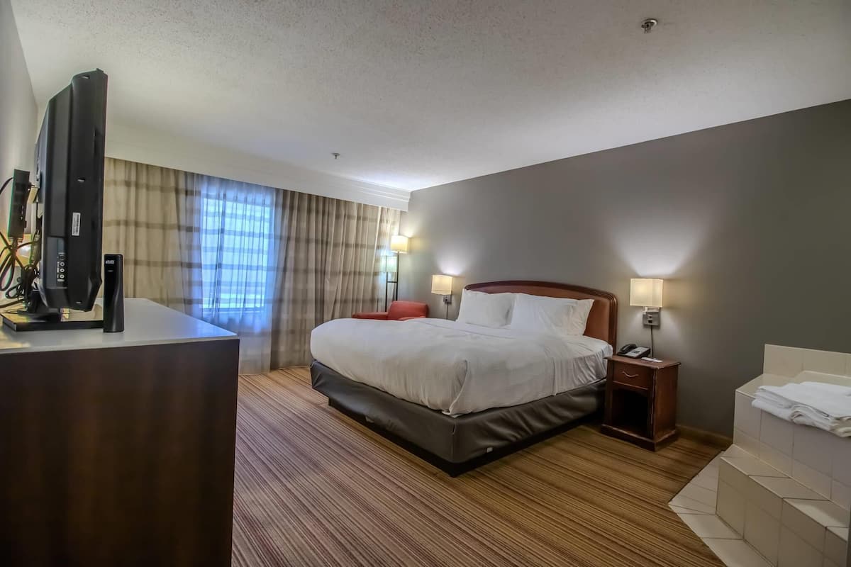 A hotel room with a bed, bedside lamps, a TV, a desk, and a bathroom with a towel rack.