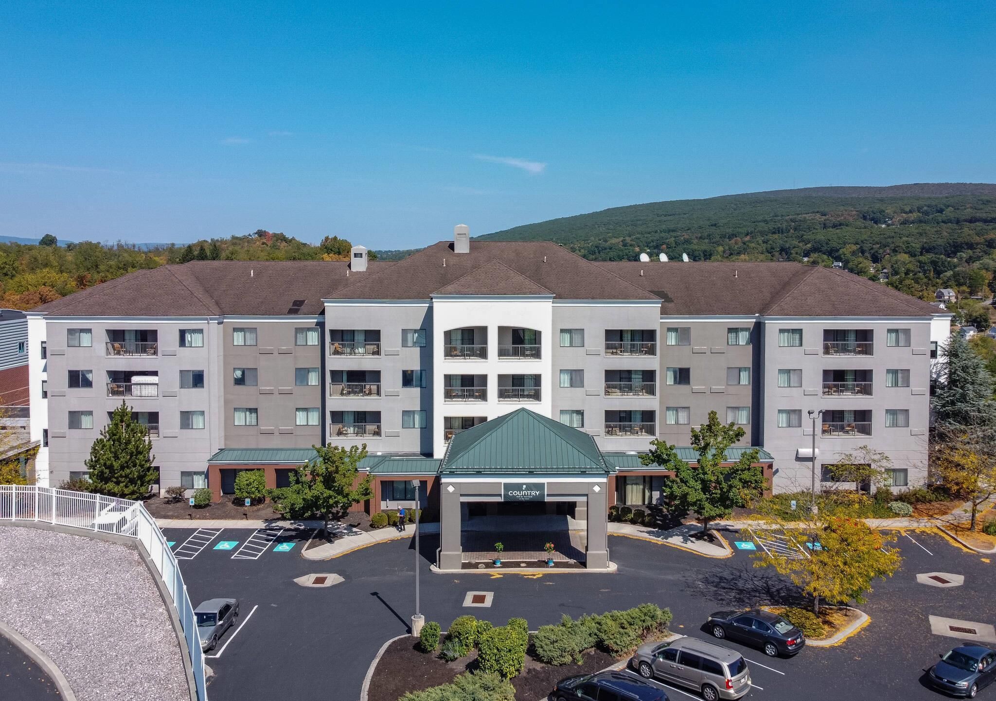 A multi-story hotel with a central entrance, parking lot, and surrounding greenery.