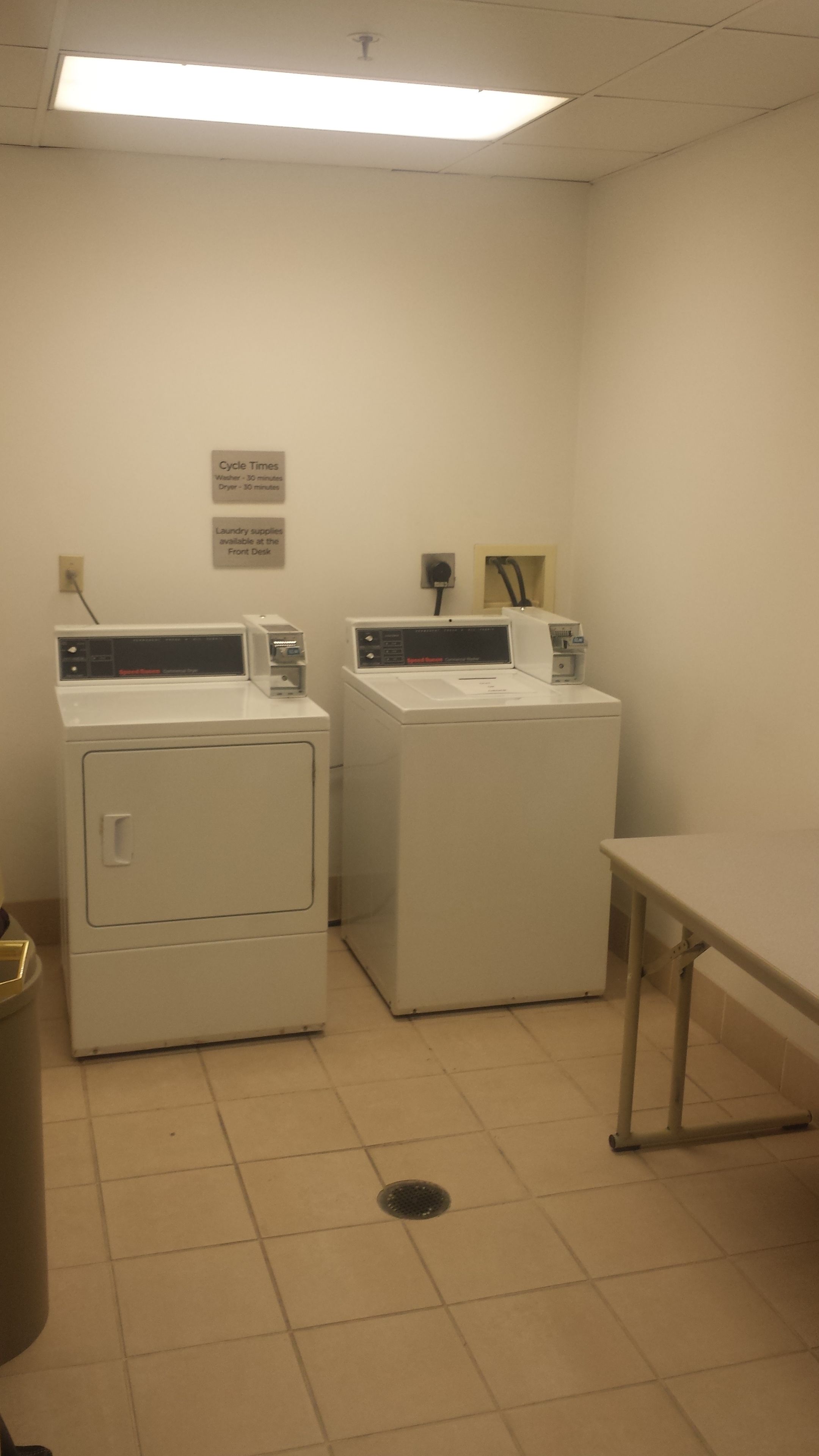 A laundry room with two front-loading washing machines, a table, and a trash can.