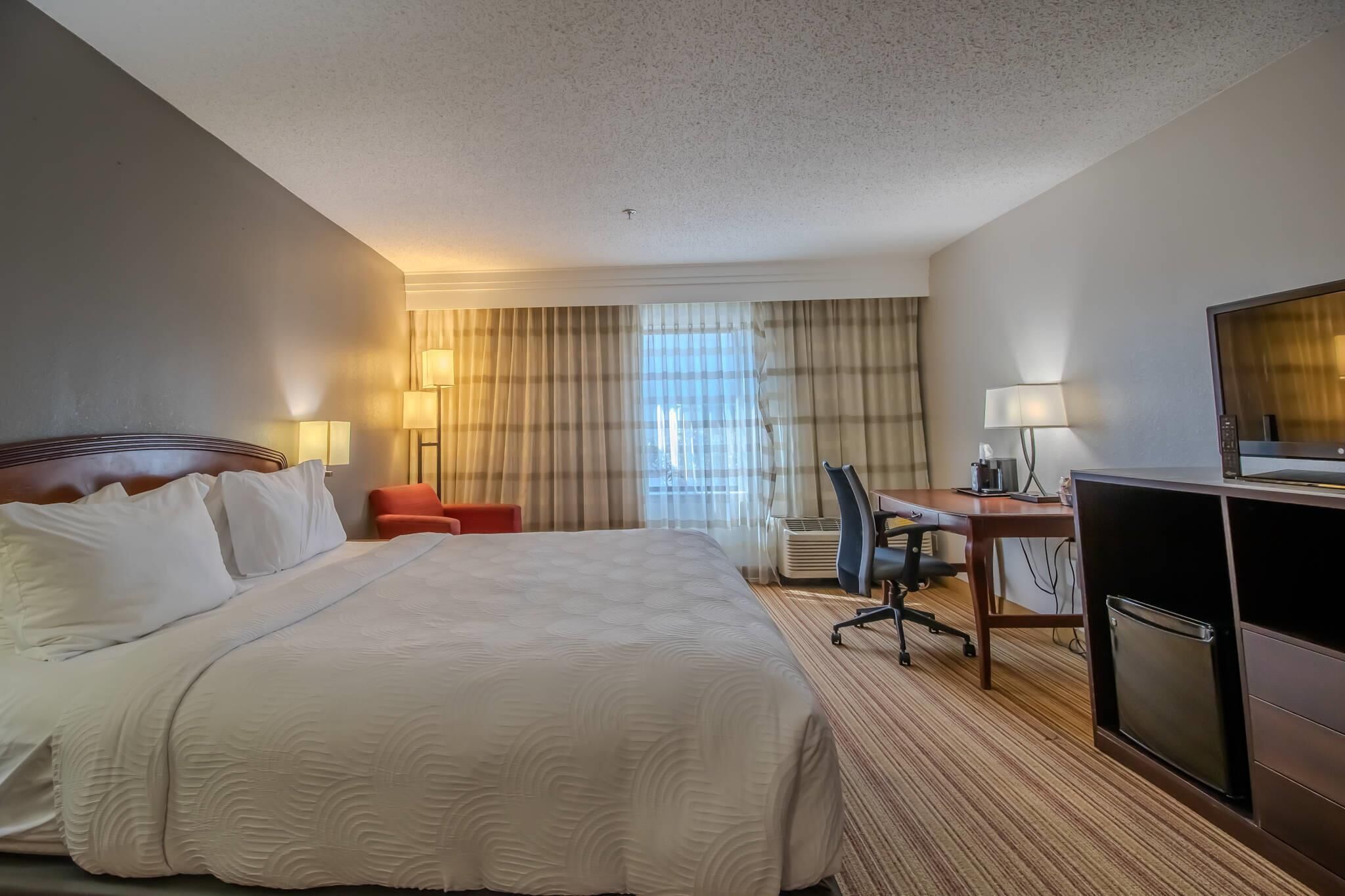 A hotel room with a large bed, a desk, a chair, a television, and a minibar.