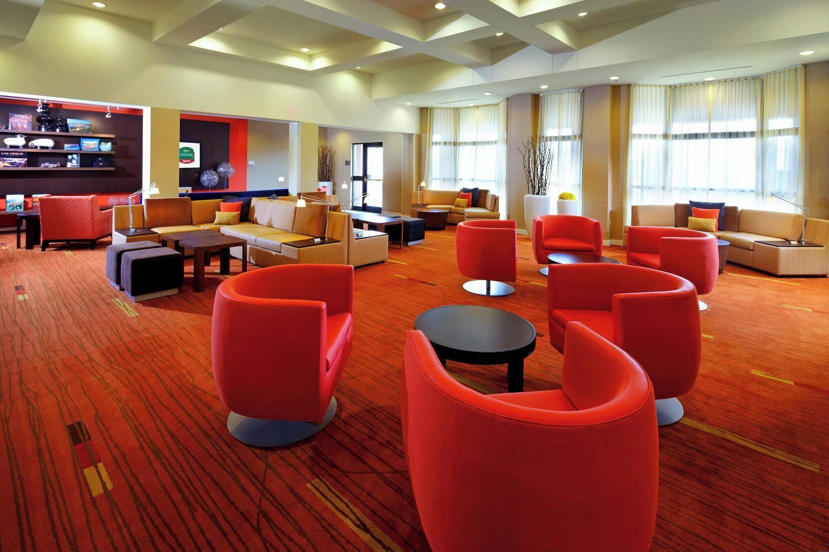 Un hall d’hôtel moderne avec des sièges rouges, un bar et de grandes fenêtres.