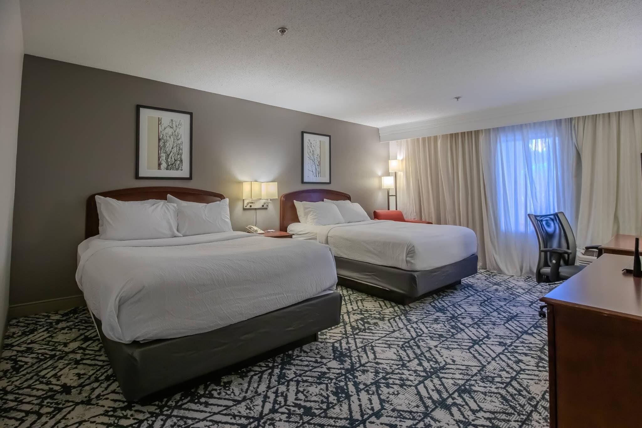 A hotel room with two beds, a desk, a chair, and two bedside lamps.