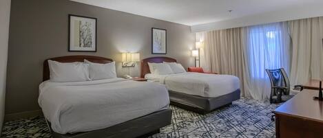 A hotel room with two beds, a desk, a chair, and two bedside lamps.