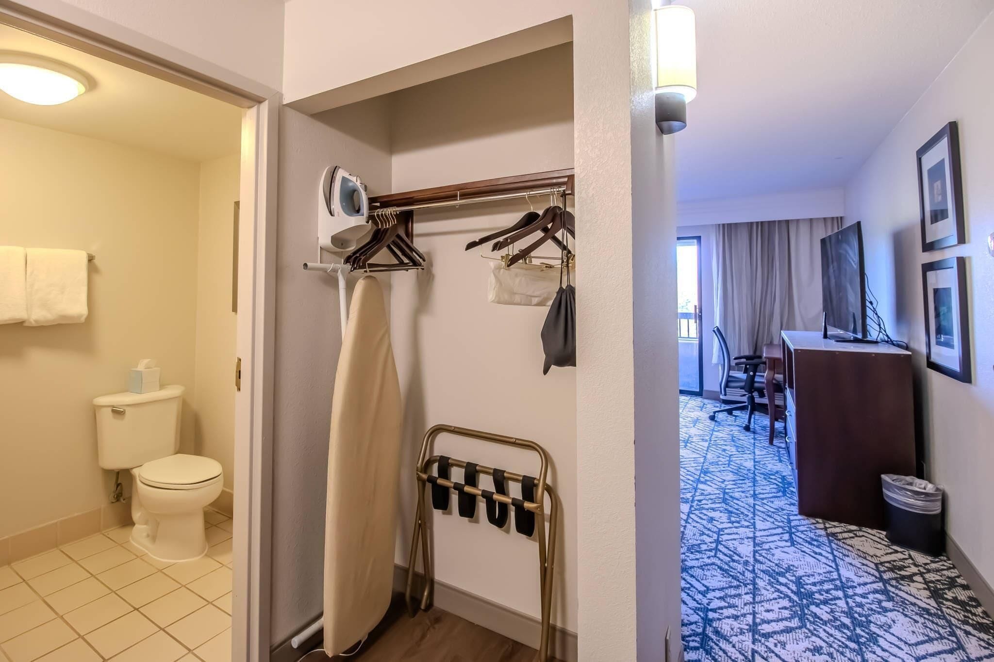 Et hotelværelse med toilet, brusebad, knagerække, skrivebord, stol og et mønstret gulv.