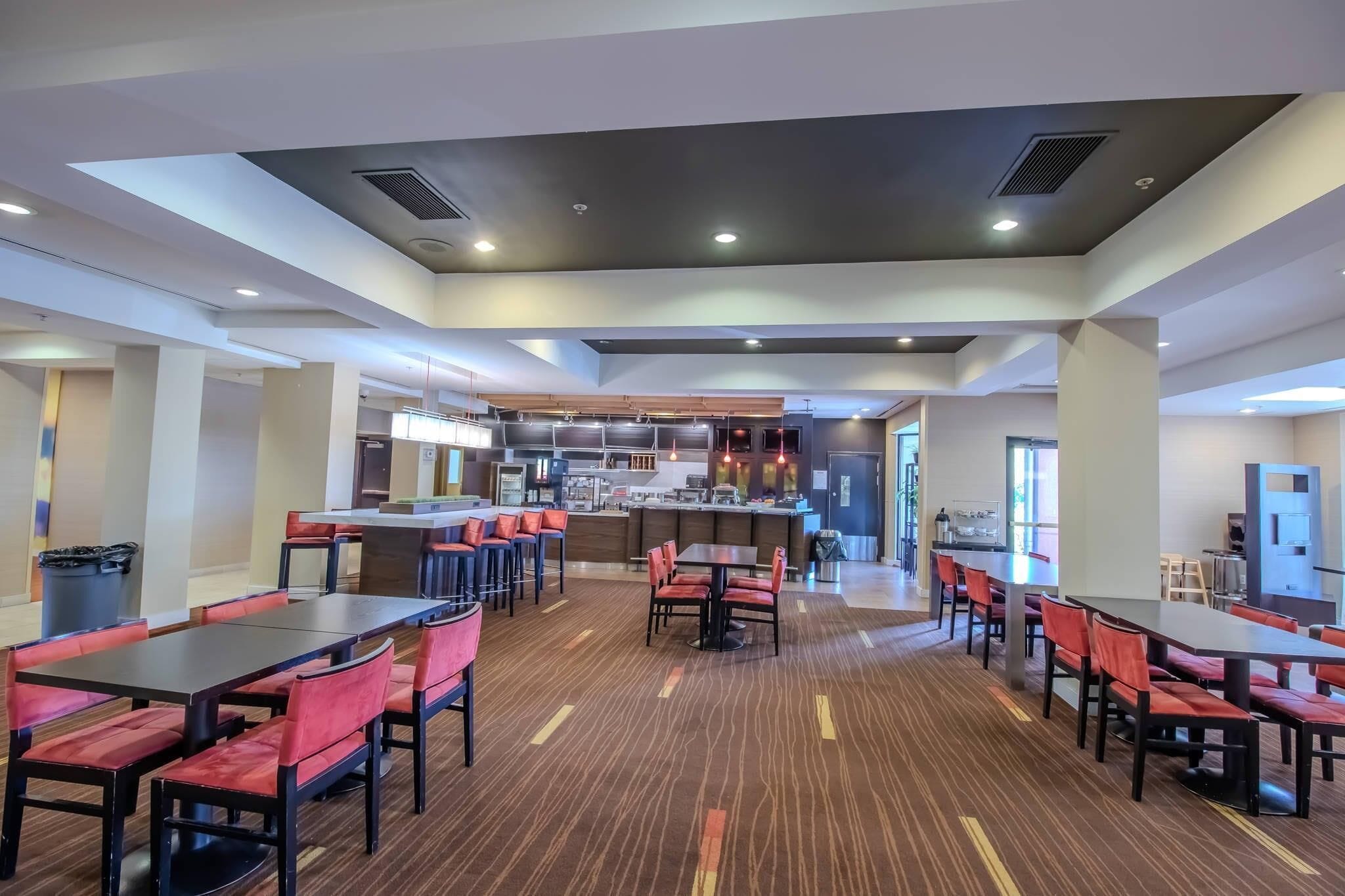 A spacious dining area with multiple tables and chairs, a central kitchen area, and a modern ceiling design.