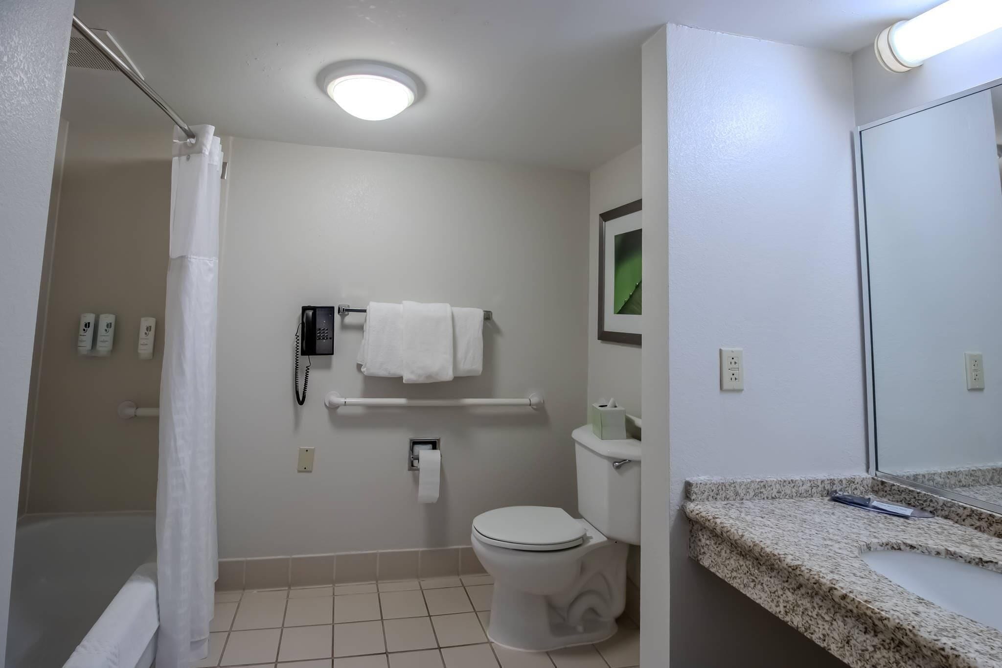 A bathroom with a toilet, a shower curtain, a towel rack, a phone, and a mirror.