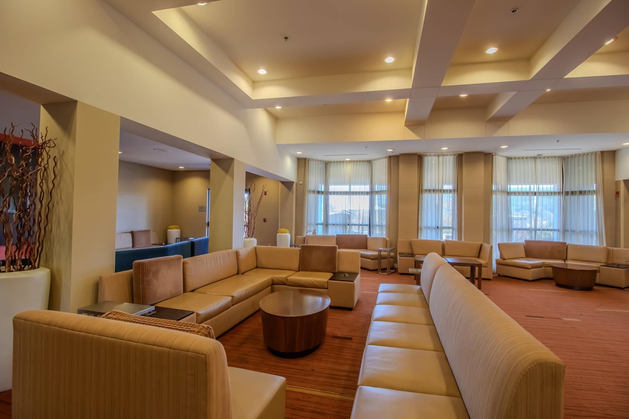 A spacious hotel lobby with a large sectional sofa, a round coffee table, and a seating area with chairs and a small table.